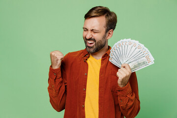 Elderly smiling cheerful man 40s years old he wears casual clothes red shirt t-shirt hold in hand fan of cash money in dollar banknotes isolated on plain pastel light green background studio portrait.