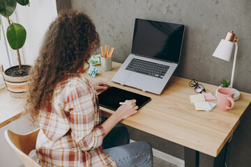 Back view young employee business woman of African American ethnicity wear casual shirt graphic designer hold in hand work use write draw stylus pc pen sit work at office desk with laptop pc computer.