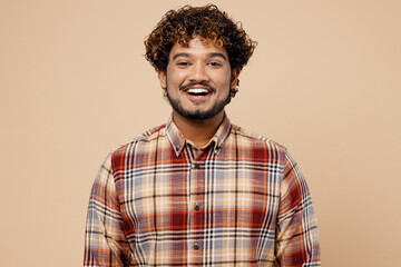 Smiling happy cheerful fun cool confident Indian man wearing brown shirt casual clothes looking camera isolated on plain pastel light beige color background studio portrait. People lifestyle concept.