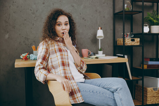 Young surprised shocked amazed smiling employee business woman of African American ethnicity wear casual shirt look camera cover mouth with hand sit work at office desk with laptop pc computer indoor