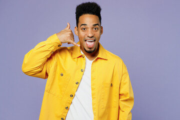 Young man of African American ethnicity wear yellow shirt t-shirt doing phone gesture like says call me back isolated on plain pastel light purple background studio portrait. People lifestyle concept.
