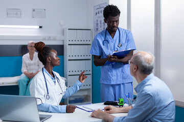 African american healthcare hospital staff reviewing senior patient record file while talking about...