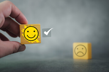 Man hand choose happy face icon on yellow wood block, The customer service satisfaction. Feedback rating and positive customer review experience. Service and satisfaction. Rating is very impressed.