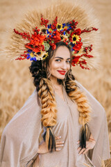 Beautiful Ukrainian young woman standing alone in a yellow wheat field. The brunette looks at the camera hugging the spikelets of wheat. Peaceful happy Ukraine.