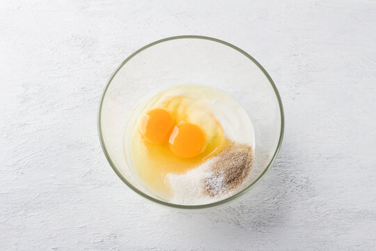 Cooking delicious semolina pie: sour cream or yogurt, two eggs, sugar, vanilla sugar and a pinch of salt in a glass bowl on a light gray background, top view