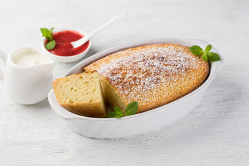Freshly prepared mannik, semolina pie in the form sprinkled with powdered sugar with sour cream and berry sauce on a light gray background