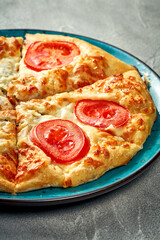 Khachapuri with salty melted cheese and tomato in a plate. Concrete background