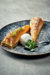 Delicious Turkish baklava with pistachios, honey and ice cream in a plate on a concrete background