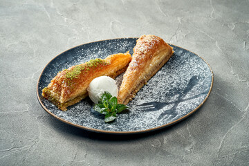 Delicious Turkish baklava with pistachios, honey and ice cream in a plate on a concrete background