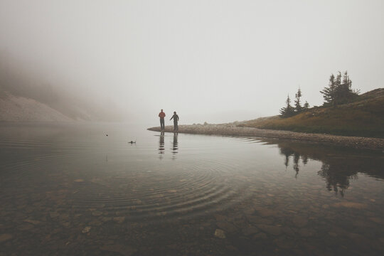 Father cheers as son skipping rock across alpine lake during father son camping trip, Merritt, British Columbia, Canada