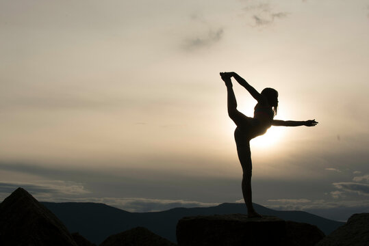 Woman practicing yoga on mountain during a cloudy sunset, North Conway, New Hampshire, USA