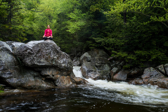 Woman practicing yoga in lotus pose on large rock in river, Gorham, New Hampshire, USA