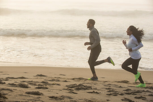 Man and woman jogging together on coastal beach during foggy day, Hampton, New Hampshire, USA