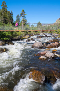 Woman jogging across rope bridge over&acirc;&euro;&nbsp;Popo&acirc;&euro;&nbsp;Agie&acirc;&euro;&nbsp;River, Sinks Canyon State Park, Lander, Wyoming, USA