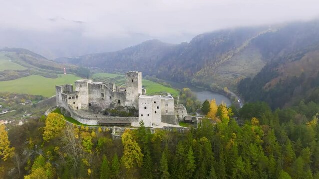 Slovak castles: an aerial view of Strečno Castle, towering on a cliff above the valley with the river Váh. Autumn, colourful leaves, mists in the valley, stone guard castle above the hilly landscape. 