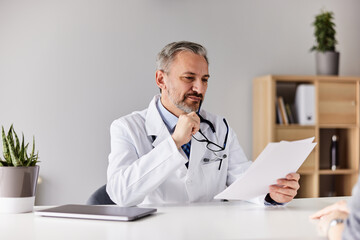 A senior doctor thinking about the results he holding while sitting at the office.