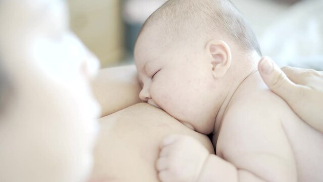 Mother caressing her 2-month-old baby while breastfeeding skin-to-skin. Then baby falls asleep suckling.