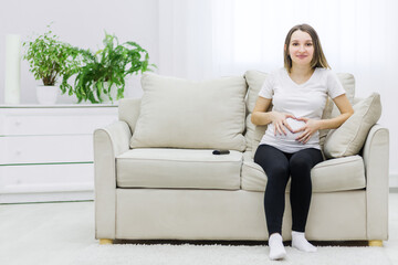 Obraz premium Photo of cute pregnant woman showing a heart with her fingers on stomach.