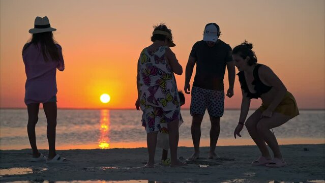 Latin family enjoying the sunset at the beach on a warm summer day looking for seashells on the sand