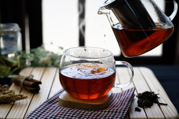 Pouring herbal hot tea into cups with steam in festive composition on table