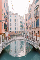 Fototapeta na wymiar A canal runs through the canyons of houses in Venice, a beautiful bridge connects the sides. The water glitters turquoise and the sun is reflected in the brick facades of the houses.