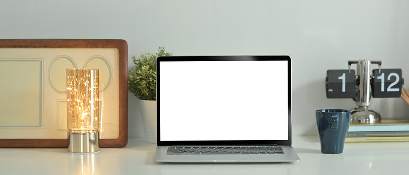 Laptop computer, coffee cup, picture frame and potted plant on white table. Blank screen for text information or content