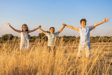 Three kids with open arms in the countryside at summer