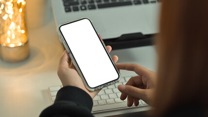 Unrecognizable woman hands holding smart phone with white screen. Over shoulder closeup view, selective focus on phone