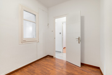 Empty spacious room well lit by daylight. The floor is dark brown wood parquet. White walls with a doorway opening onto a corridor. Through the open door you can see part of the rest of the apartment.