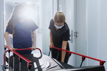 Two nurses roll an empty hospital gurney down the corridor. Emergency call.