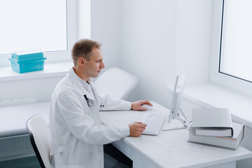 A male doctor is sitting at a computer in his office. Modern medical care in the clinic.