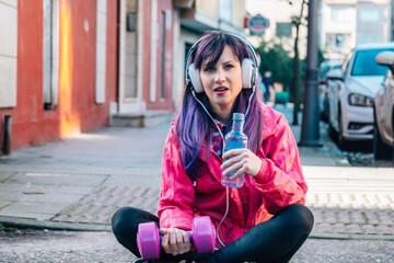 sporty woman with headphones resting with dumbbells and bottle of water