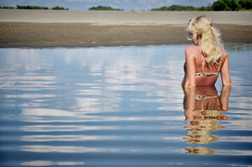 A girl with blonde hair stands chest-deep in a lake on a summer day