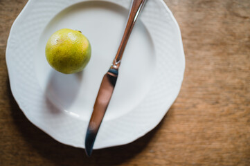 Eine einzelne Limette und ein Messer liegen auf einem weißen Teller auf einem Holztisch.