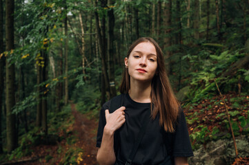 Portrait of attractive female tourist in casual clothes with backpack on back and looking at camera with serious face