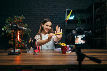 Positive female blogger showing makeup to camera while shooting video tests, looking at camera with...