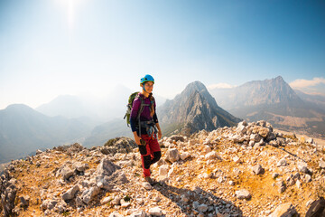 young girl climber in a helmet and with a backpack walks along a mountain range against the backdrop of mountains and climbing and hiking.