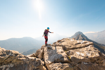 young girl climber in a helmet and with a backpack walks along a mountain range against the...