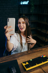 Smiling girl streamer gamer in headset plays online games in meridian and takes selfie on...