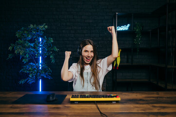 Portrait of a joyful woman in a headset sitting at a computer at home and playing online games and...