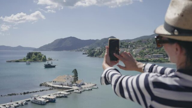 Tiourist woman take picture with smartphone from aerial view of Vlacherna Monastery Kanoni and Mouse islands, slow motion