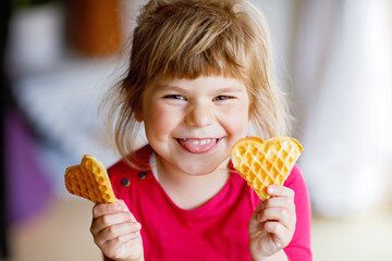 Portrait of happy little preschool girl holding fresh baked heart waffle. Smiling hungry toddler...