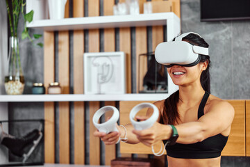 A smiling female uses a VR device, headset, and controllers for fun after the workout.
