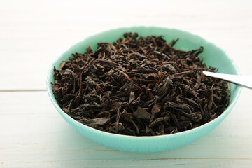 Fototapeta na wymiar Dry black tea leaves in bowl on white background
