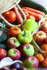 Straw bag and reusable fabric bags filled with various healthy fruit and vegetables. Wooden background, selective focus.