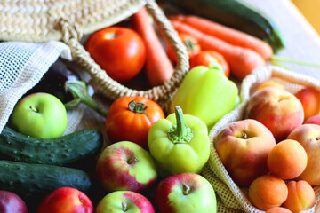 Straw bag and reusable fabric bags filled with various healthy fruit and vegetables. Wooden background, selective focus.