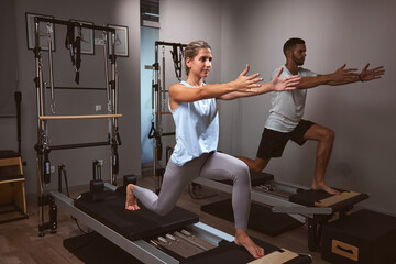 Young woman and man exercising in a gym with personal trainer on pilates machine.