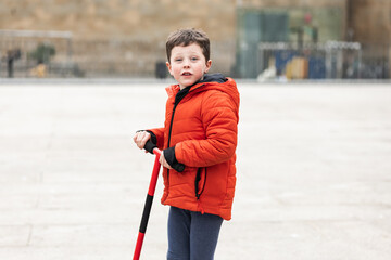 elementary Caucasian boy playing with scooter in the square