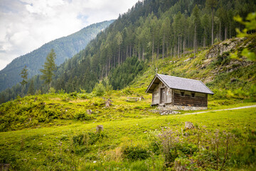 small mountain house in green meadow with forest in the background some clouds