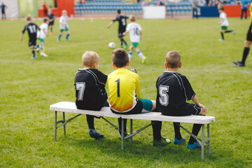 Young boys in soccer jerseys sitting on the substitute players' bench. Children play sports during...
